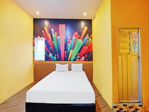 A hotel room with a bed, a colorful abstract painting on the wall, and a door with a floral design.