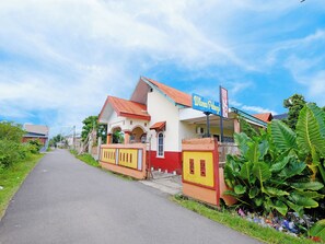 A building with a sign that reads 'Wisma Pelangi' and a paved road leading to it. - OYO 90977 Wisma Pelangi Palopo (Palopo)