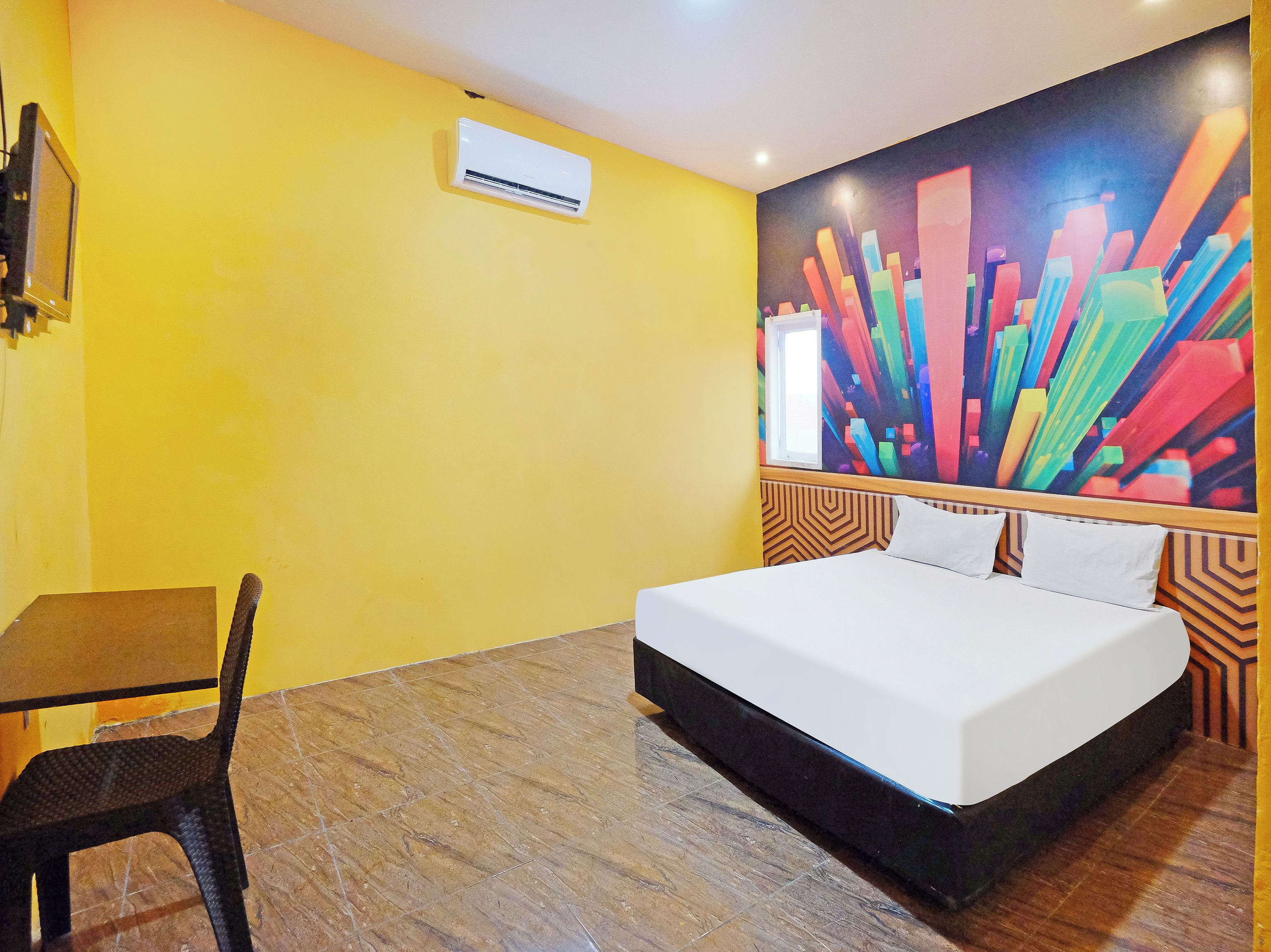 A hotel room with a bed, a chair, a desk, and a colorful abstract painting on the wall.