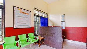 A waiting area with green chairs, a wooden table, and a bulletin board with a notice. - OYO 90977 Wisma Pelangi Palopo (Palopo)