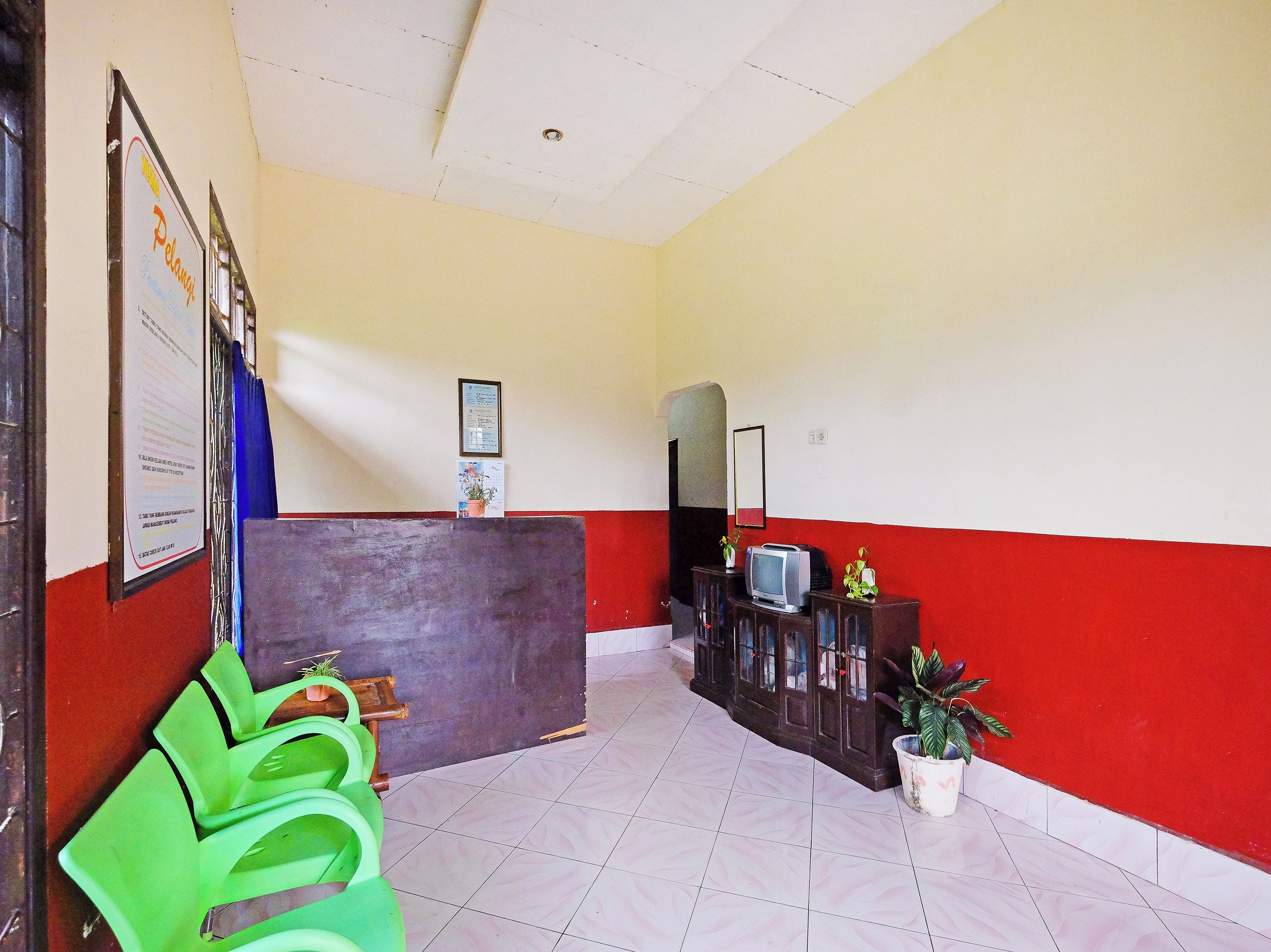 Un área de recepción con mostrador, espejo, televisor y plantas en macetas.