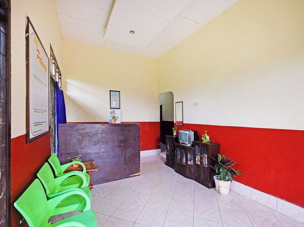 Uma área de recepção com balcão, espelho, televisão e plantas em vasos.