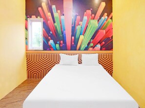 A hotel room with a bed, a window, and a colorful abstract painting on the wall. - OYO 90977 Wisma Pelangi Palopo (Palopo)
