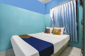 Una cama bien hecha con una colcha azul y blanca, dos almohadas estampadas y una manta azul.