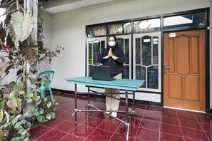 A person standing by a table with a laptop, a wooden door, and a window with curtains.