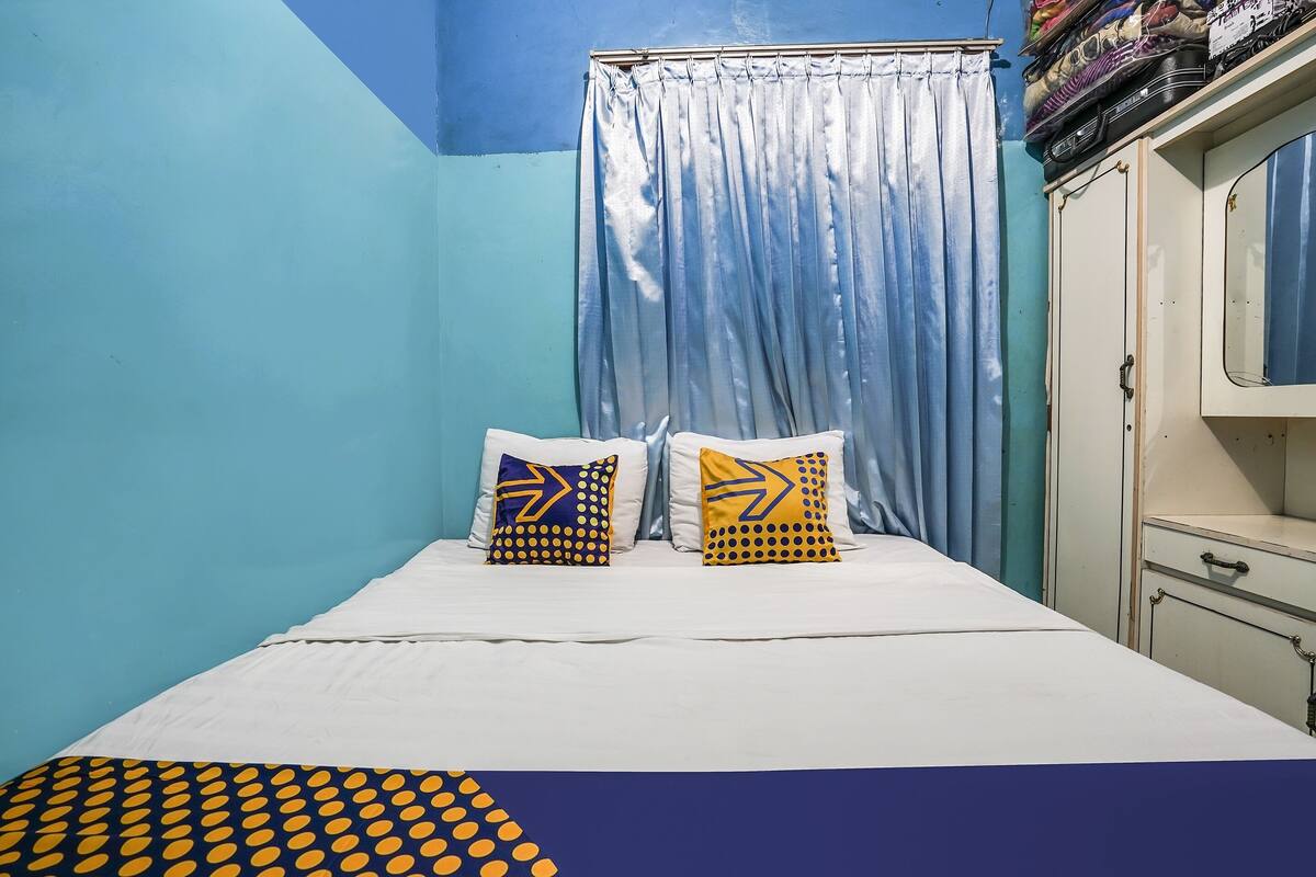 Un dormitorio con una cama, dos almohadas de diseños geométricos, una cortina azul y un armario.