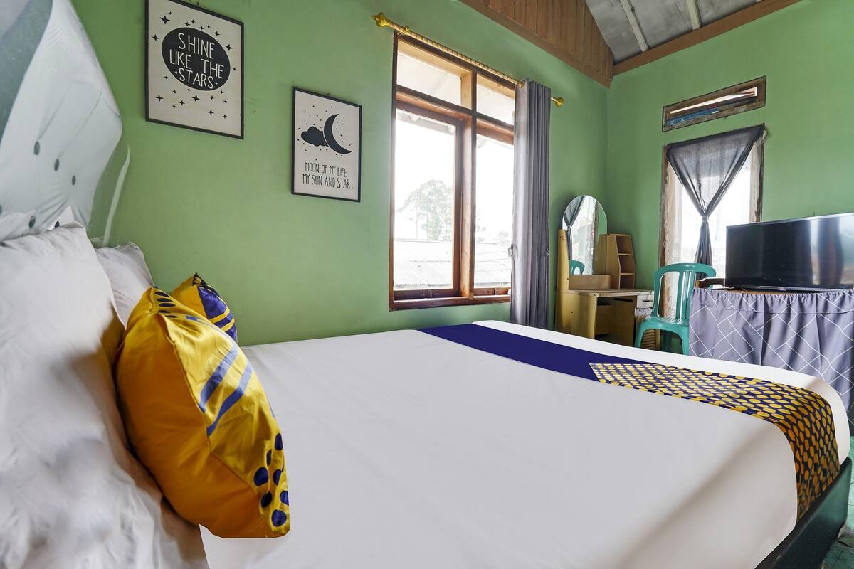 A room with a bed, a window, a TV, and a wall with a framed picture.