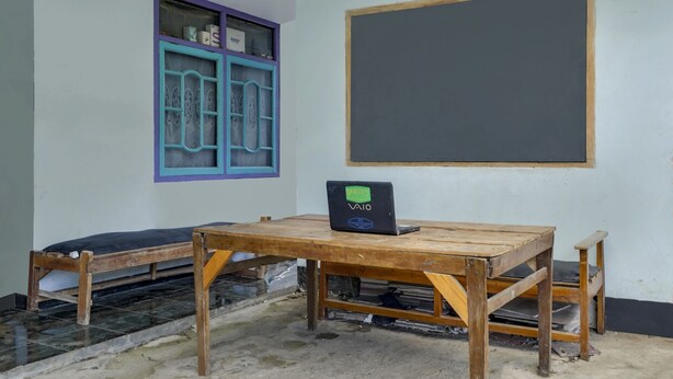 A classroom with a wooden table, a blackboard, and a window with a blue frame. - OYO 91011 Eco Tourism Desa Cibodas Areng 1 Syariah (Lembang)