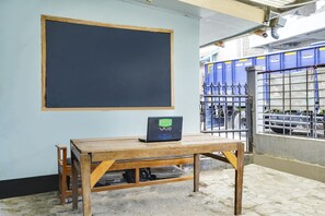 Une salle de classe avec un tableau noir, une table en bois sur laquelle se trouve un ordinateur portable, et une fenêtre dotée d’une grille métallique.