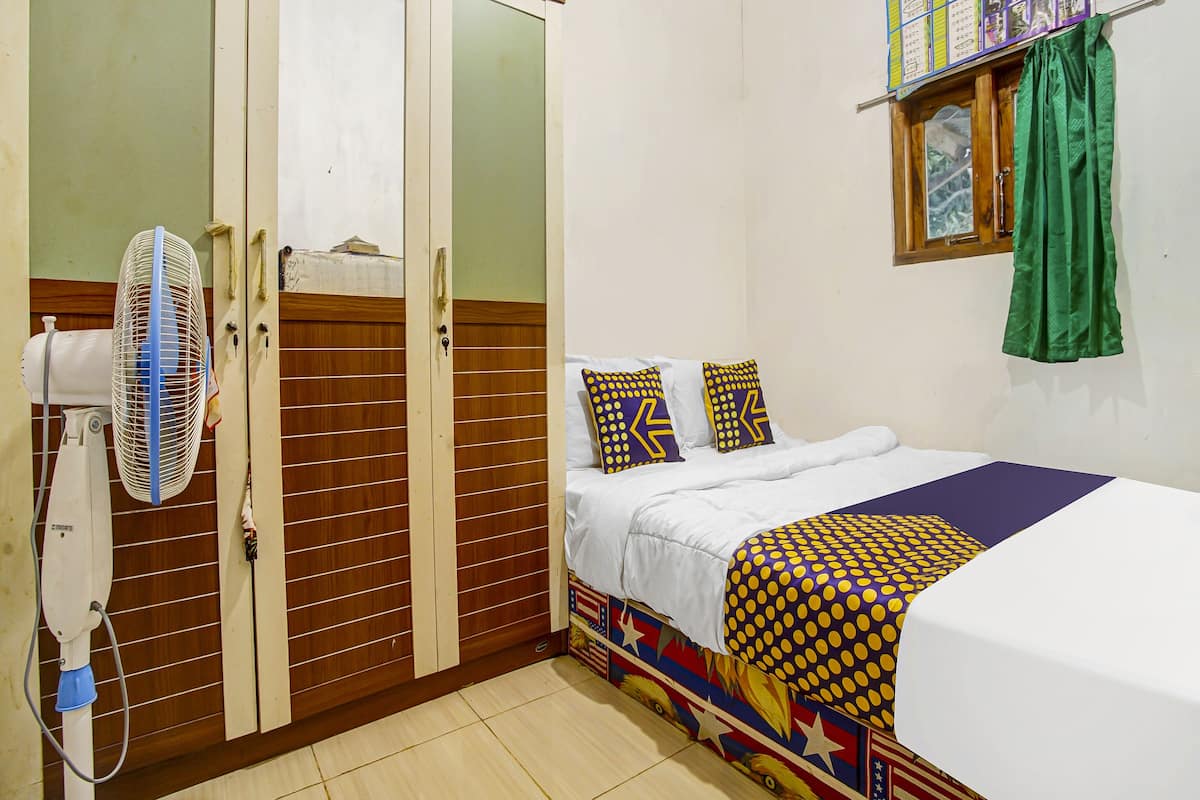 Une chambre à coucher avec un lit, un ventilateur, une armoire et une fenêtre avec des rideaux.