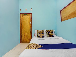 A bedroom with a wooden door, a bed with white bedding, and patterned pillows. - OYO 91089 Desa Wisata Air Terjun Way Kalam Syariah (Kalianda)