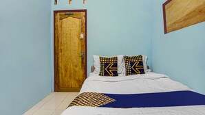 A bedroom with a wooden door, a bed with white bedding and patterned pillows, and a blue wall. - OYO 91089 Desa Wisata Air Terjun Way Kalam Syariah (Kalianda)
