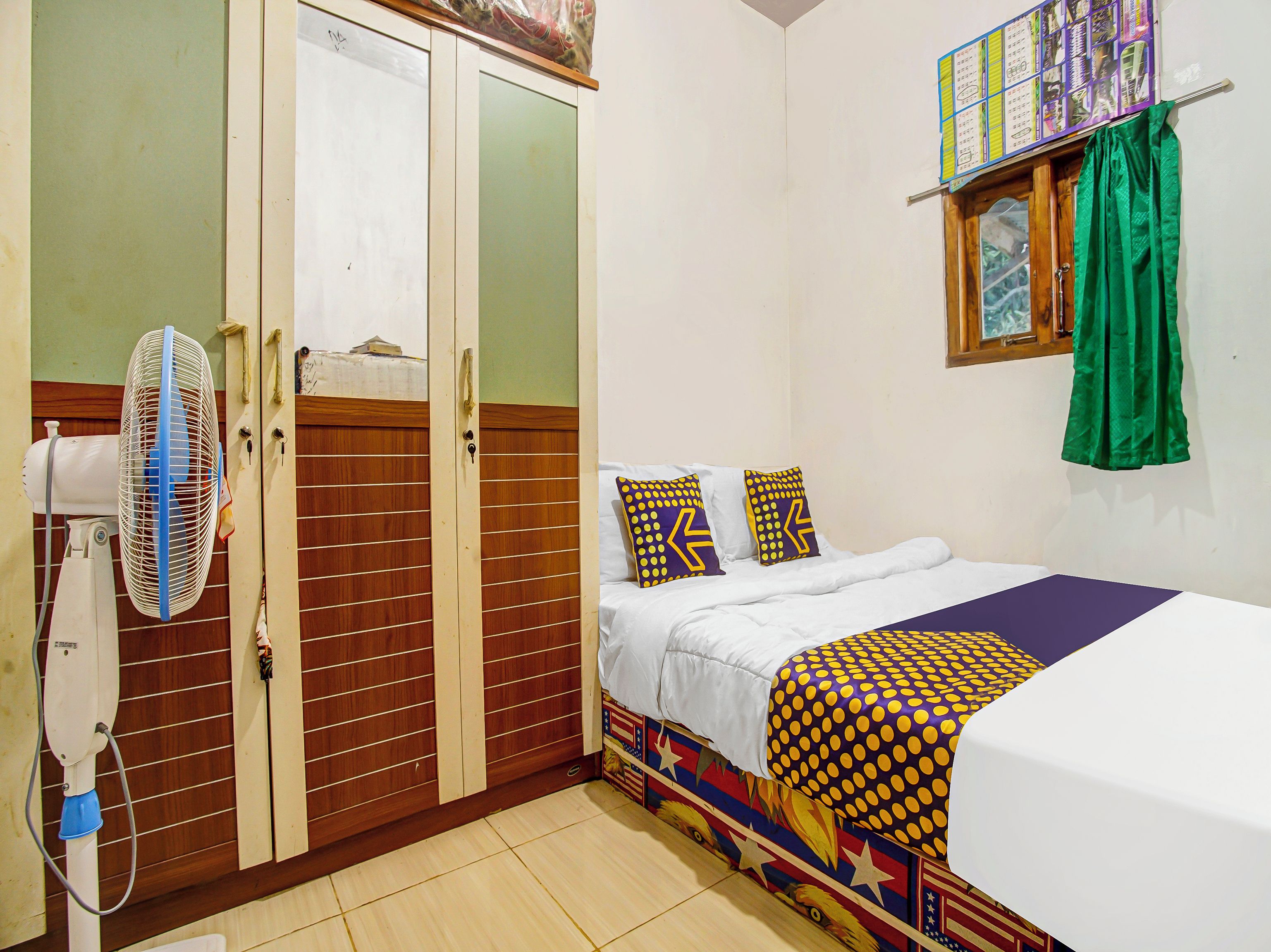 A bedroom with a bed, a fan, a wardrobe, and a window with curtains.