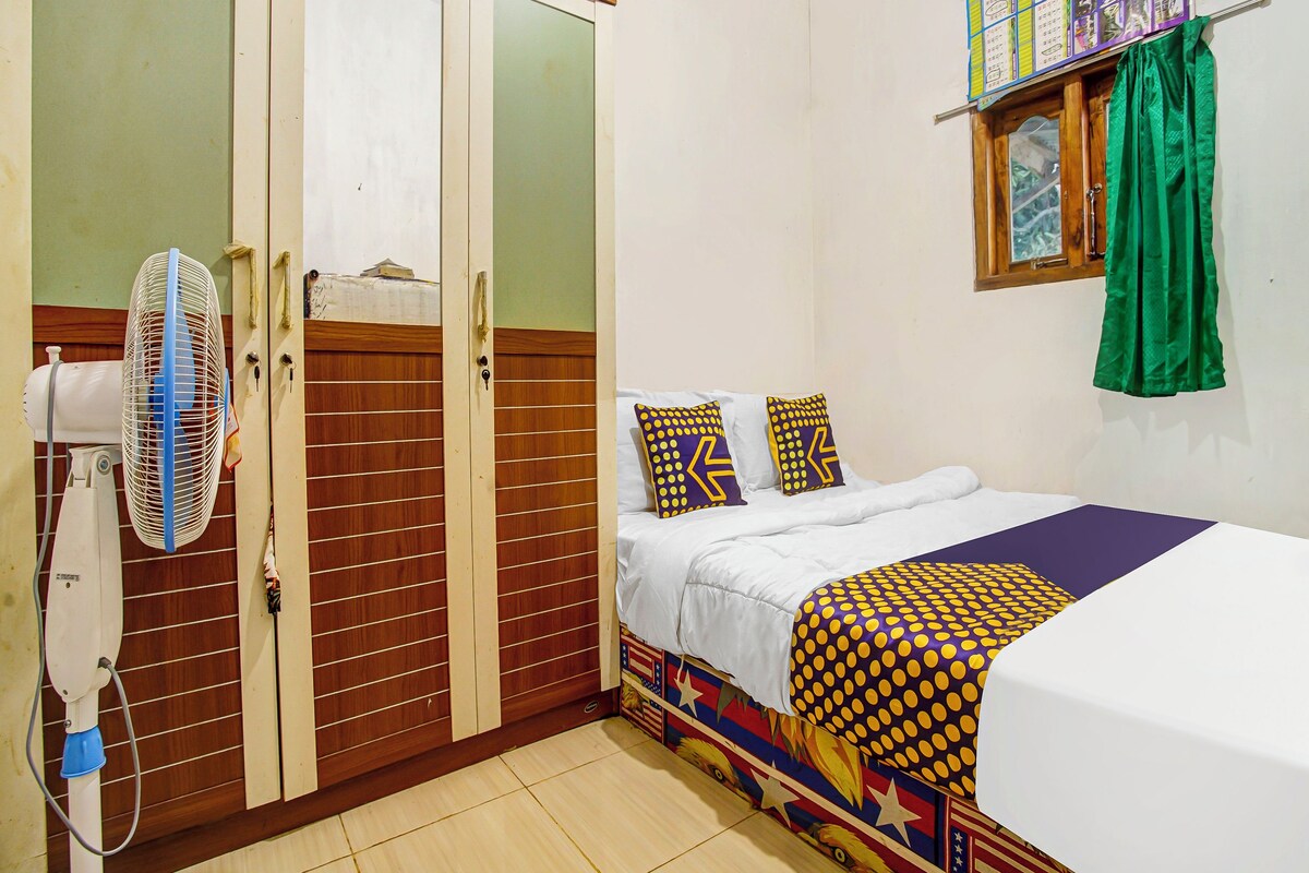 A bedroom with a bed, a fan, a wardrobe, and a window with curtains.