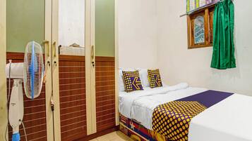 A bedroom with a bed, a fan, a wardrobe, and a window with curtains.