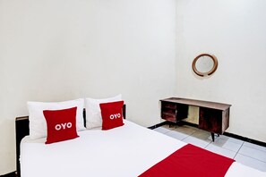 Une chambre d’hôtel avec un lit, deux oreillers rouges portant la marque « OYO », une table de chevet en bois et un miroir rond accroché au mur.