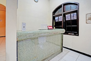 A reception desk with a laptop and a QR code sign, a clock on the wall, and a window with a view of the outside.