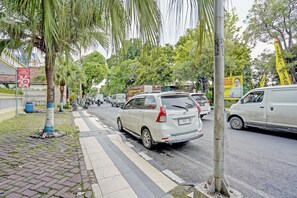 A street with parked cars, palm trees, and a building with a sign. - OYO 91198 Hotel Mahkota 2 Lamongan (Lamongan)