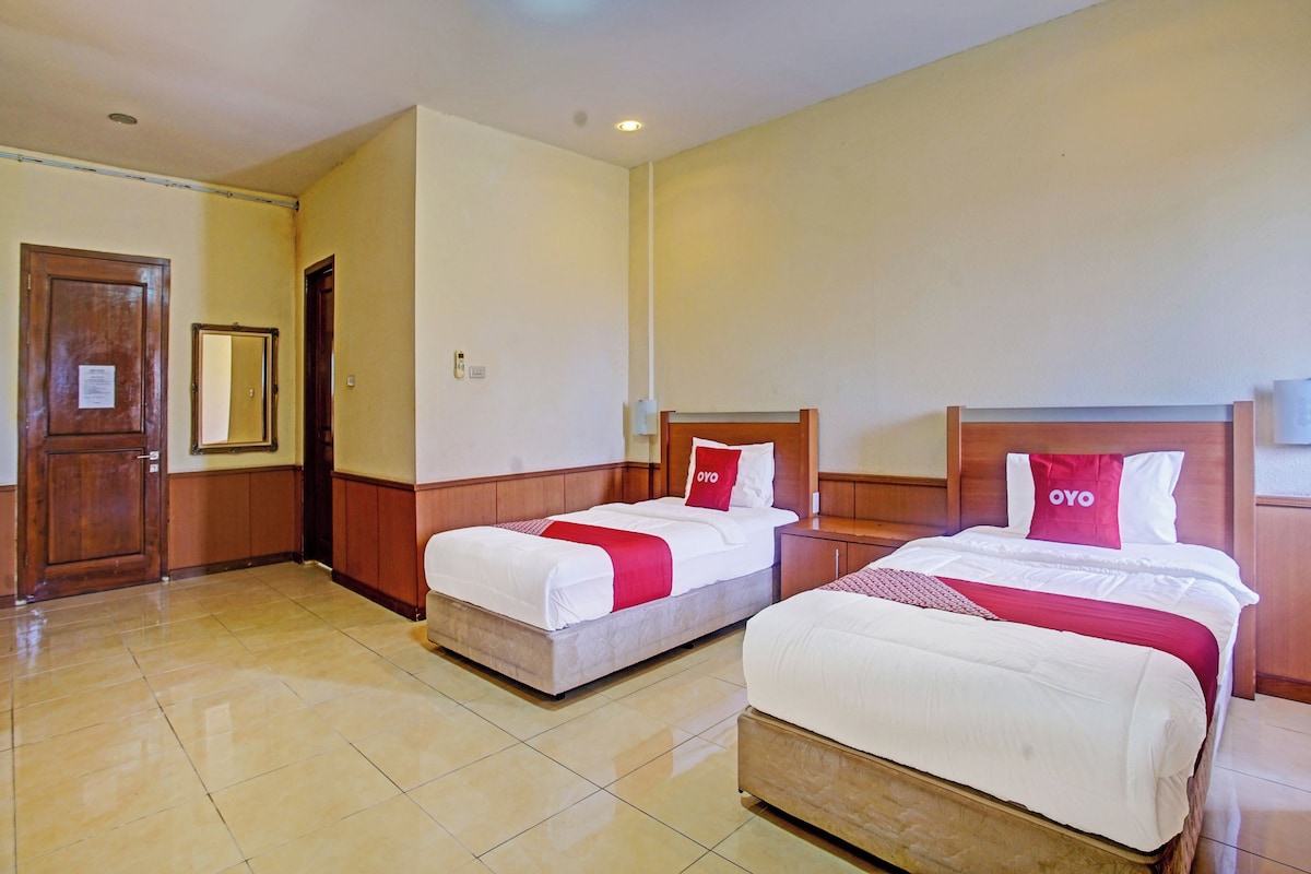A hotel room with two beds, a wooden door, a mirror, and a tiled floor.