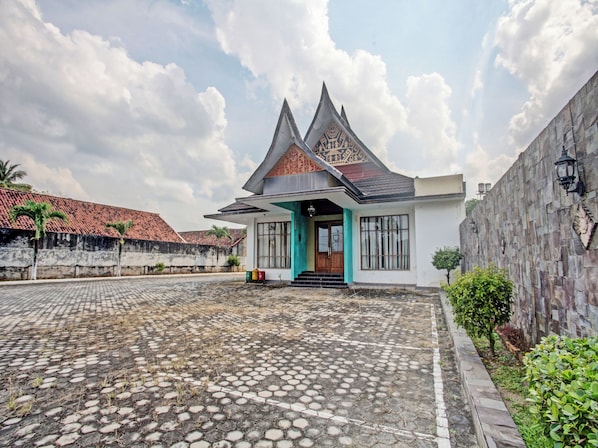 A traditional house with a tiled roof, a front porch, and a stone wall. - OYO 90947 Hotel Sarbini (Menggala)