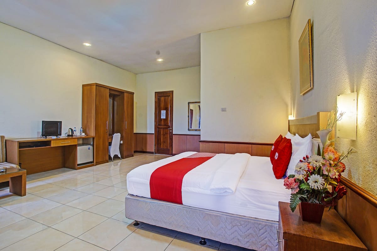 A hotel room with a bed, a desk, a chair, a small refrigerator, and a mirror on the wall.