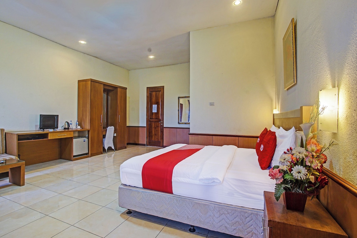 Quarto de hotel com cama, escrivaninha, cadeira, um pequeno frigorífico e espelho na parede.