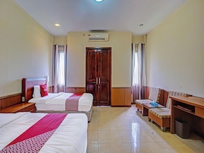 A hotel room with two beds, a wooden wardrobe, a bench, a desk, and a trash bin. - OYO 90947 Hotel Sarbini (Menggala)
