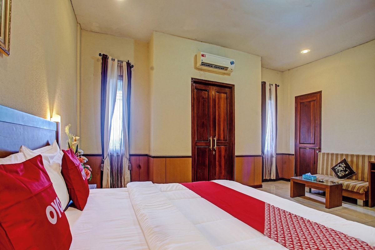A hotel room with a large bed, a wooden wardrobe, a small table, and an air conditioning unit on the wall.
