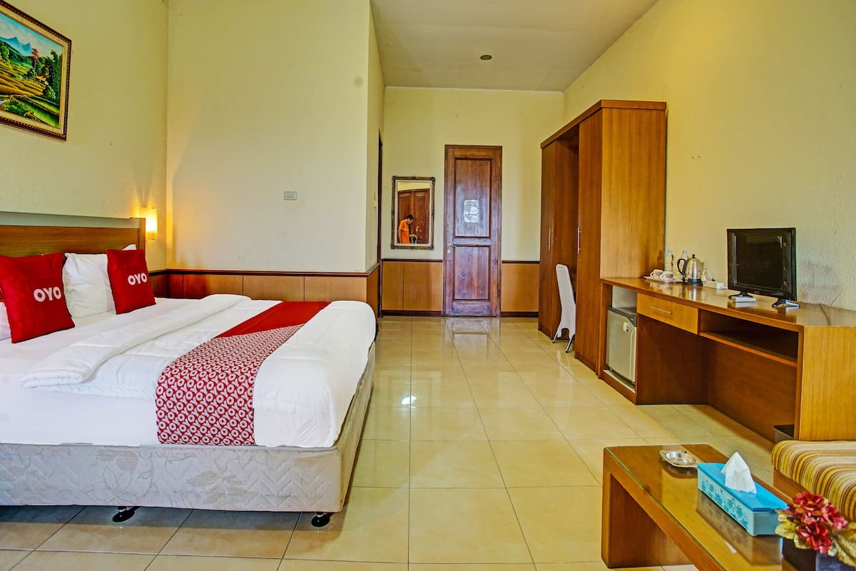 A hotel room with a bed, a desk, a television, and a bathroom visible in the background.