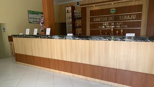 A reception desk with a wooden finish and a marble top. There are several trophies displayed on shelves behind the desk. - OYO Home 91250 Desa Wisata Taraju (Taraju)