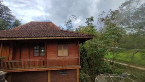 A two-story wooden house with a tiled roof, a balcony, and a view of a lush green landscape. - OYO Home 91250 Desa Wisata Taraju (Taraju)