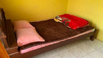 A single bed with a brown mattress, pink and white patterned pillows, and a red blanket.