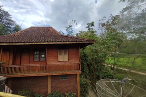 Ein zweistöckiges Holzhaus mit Ziegeldach, einem Balkon und Blick auf eine üppige grüne Landschaft.