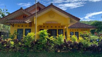 A yellow building with a tiled roof, surrounded by lush greenery.
