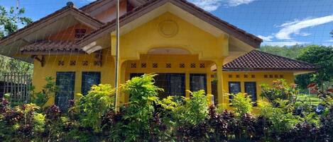 A yellow building with a tiled roof, surrounded by lush greenery.