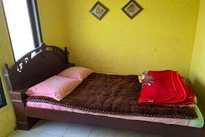 A single bed with a headboard, a pink pillow, a brown blanket, and a red blanket on the side.
