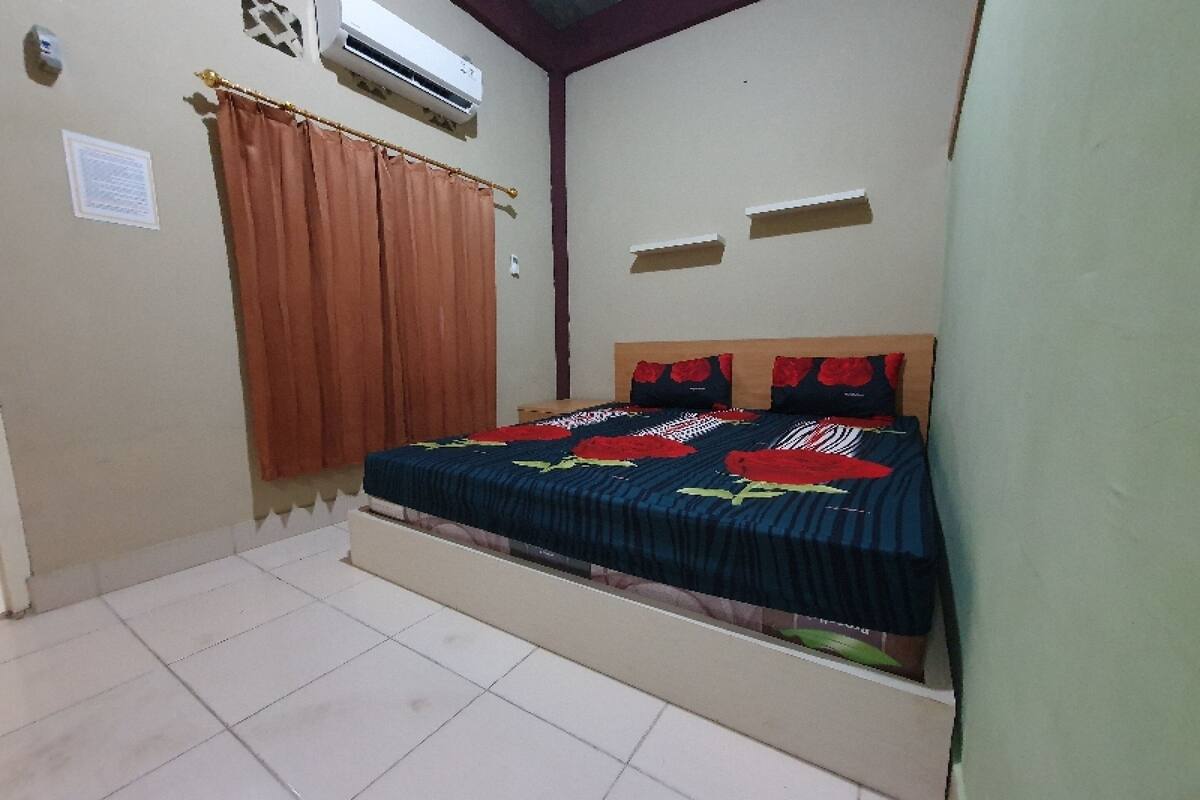 Une chambre à coucher avec un lit, des rideaux, un climatiseur et un sol carrelé.