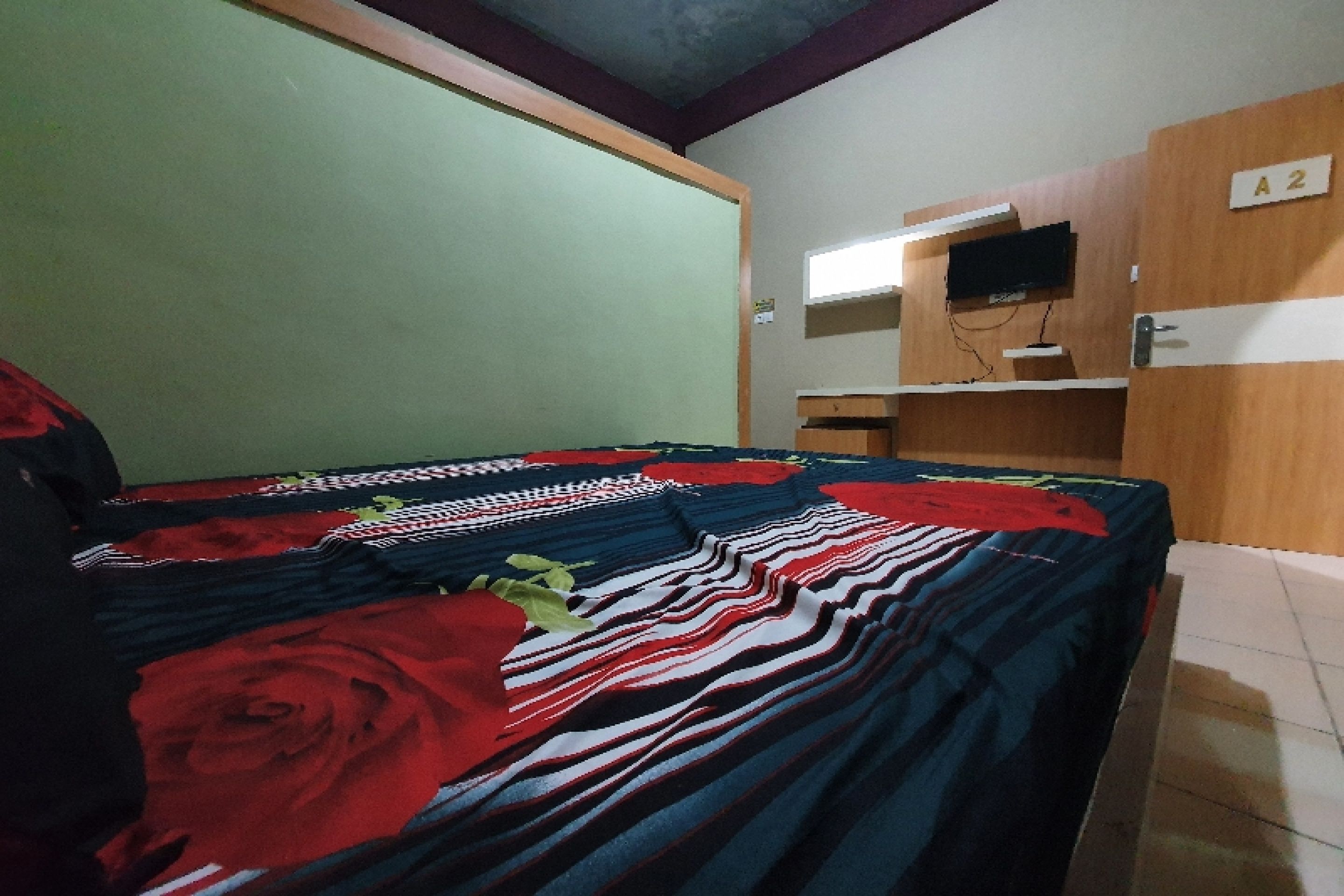 A room with a bed covered in a striped blanket, a wooden wardrobe with a television, and a green wall.