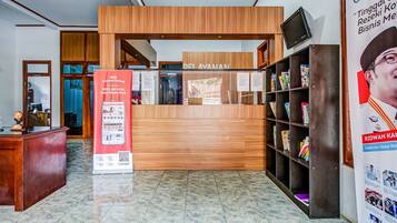 A reception desk with a wooden counter, a red sign, and a bookshelf with various items.