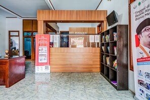Una recepción con mostrador de madera, un letrero rojo y una estantería con diversos objetos.