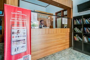 A reception desk with a wooden finish, a large red sign advertising OYO membership, and a bookshelf filled with books. - OYO Homes 91124 Desa Wisata Kaso (Kaso)