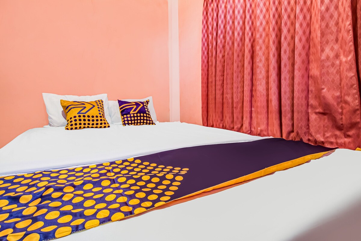 A bed with a white mattress, a purple and yellow patterned bedspread, and two pillows with geometric designs.