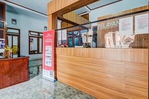 Un mostrador de recepción con detalles de madera, una mampara de vidrio y un cartel con texto.