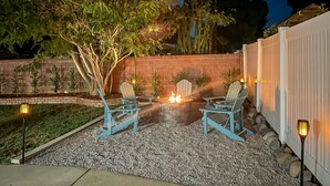 An outdoor patio with a fire pit, two Adirondack chairs, and a brick wall.