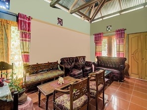A living room with a high ceiling, wooden furniture, and patterned curtains.