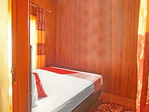 A single bed with a patterned bedspread, a wooden wall, and a patterned rug on the floor.