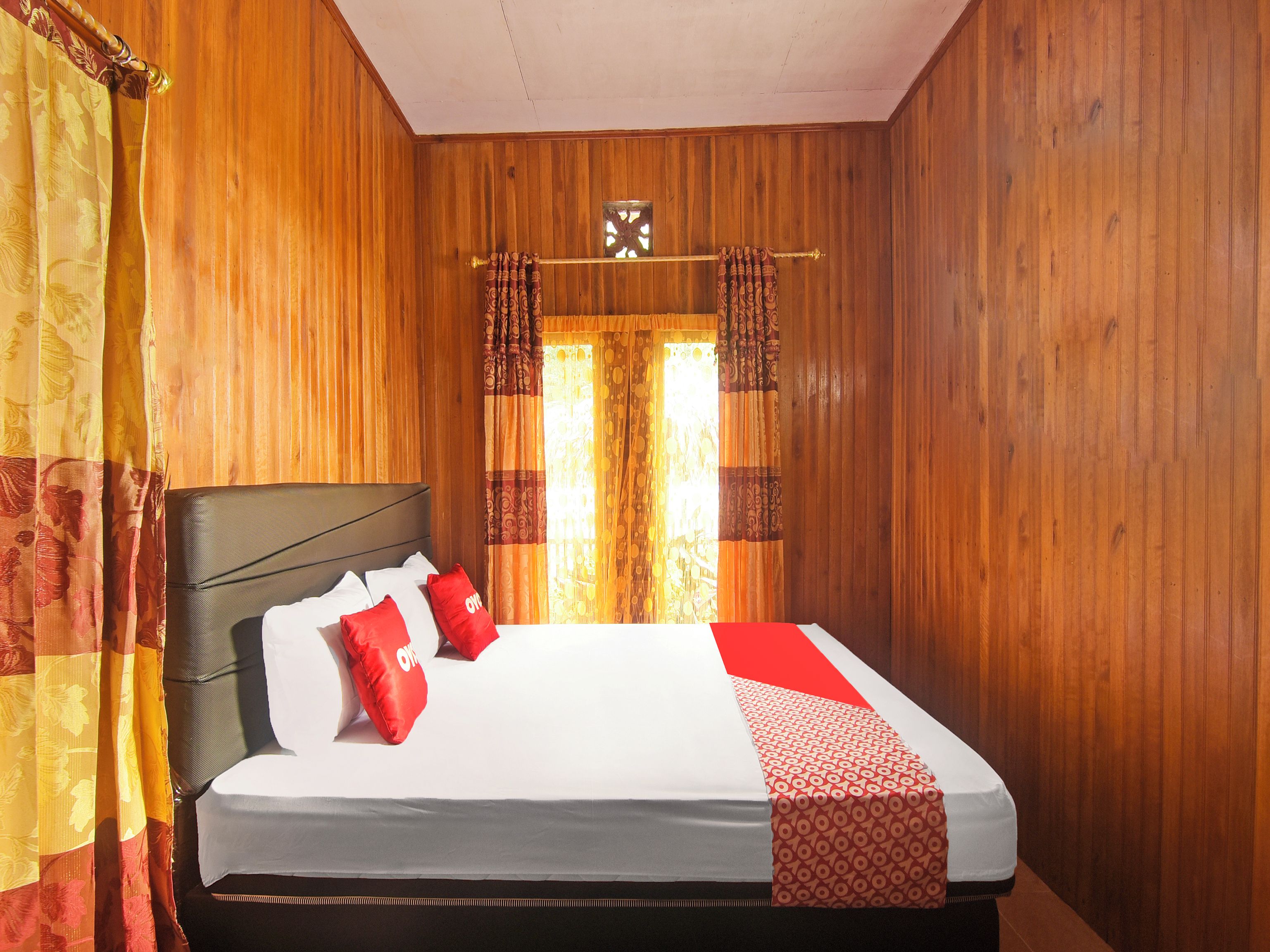 Una habitación con paneles de madera, una cama, cortinas y un ventanal con cortinas estampadas.