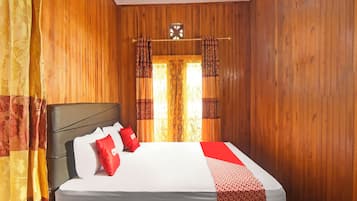 Una habitación con paneles de madera, una cama, cortinas y un ventanal con cortinas estampadas.