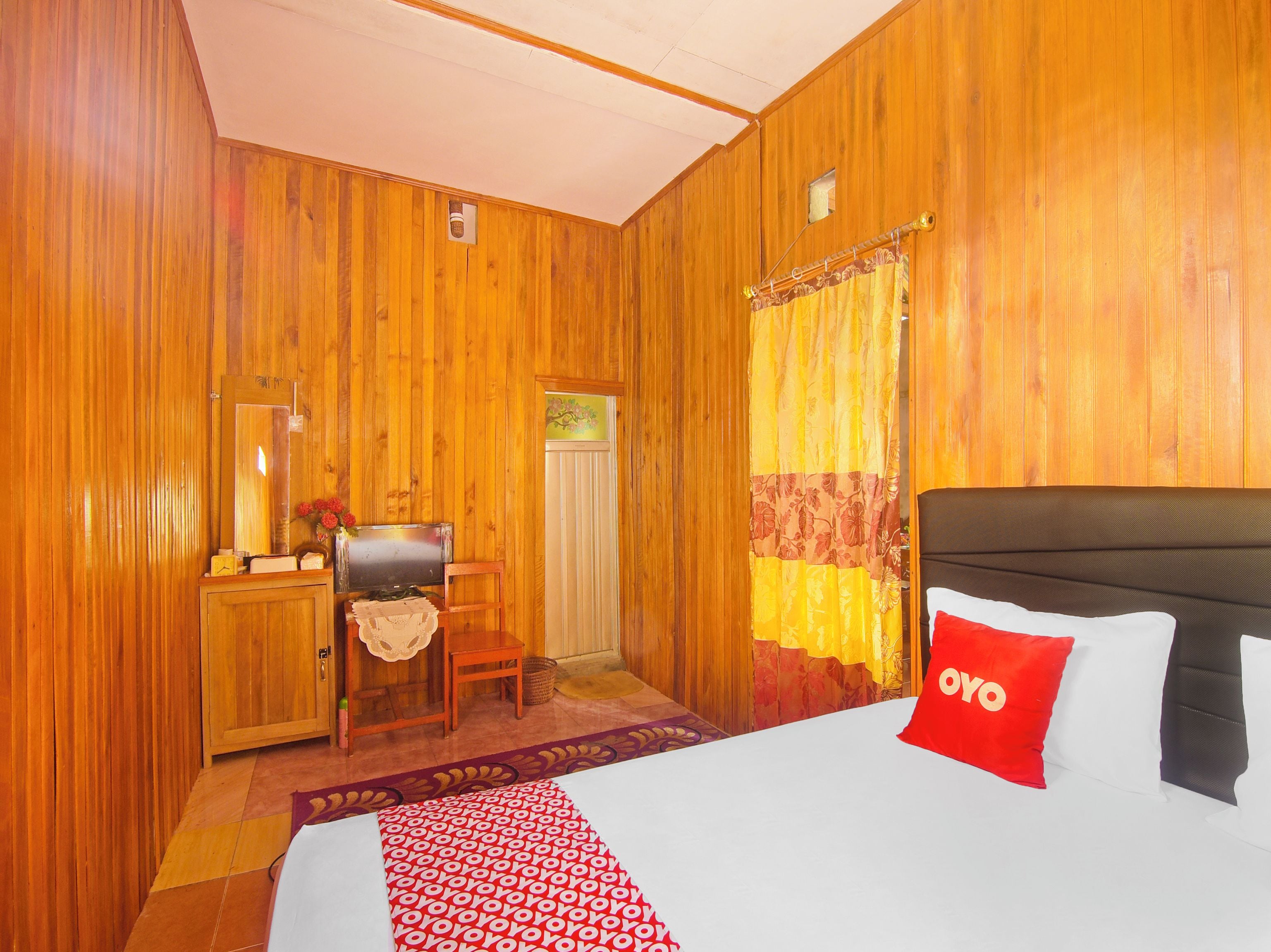 A wooden-paneled room with a bed, a desk, a chair, and a window with curtains.