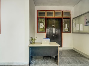 Ein Zimmer mit Schreibtisch, Laptop, Blumentopf und einer Tür mit Fenster.